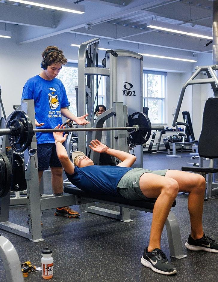 two students spot each other in the weight room